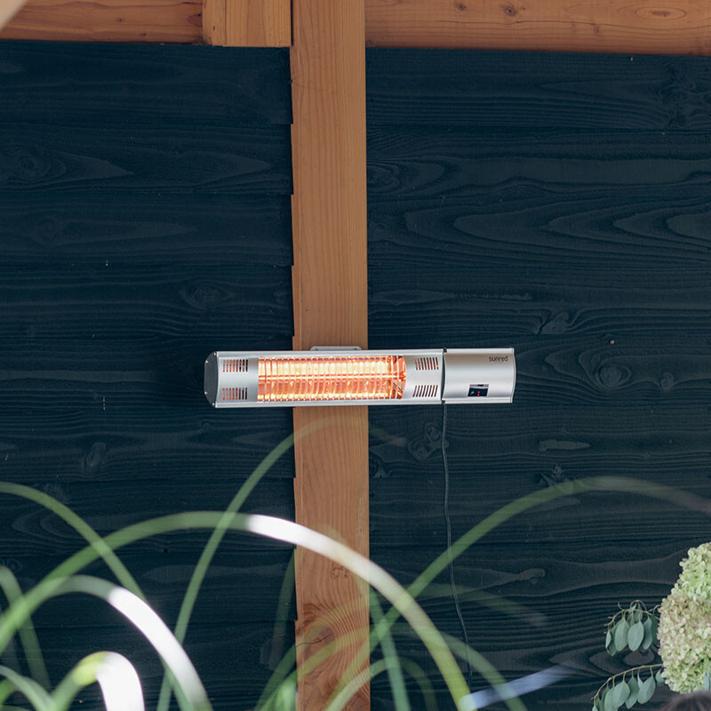 De Sunred Terrasverwarmer Ultra Wand Silver 2000 Watt hangt in de tuin.